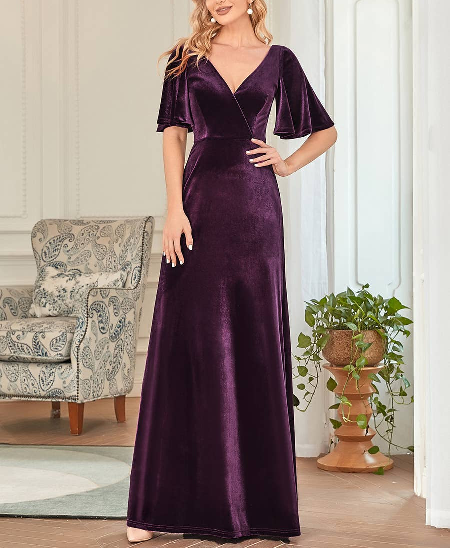 Woman wearing a purple velvet dress in a room with a chair and plant.