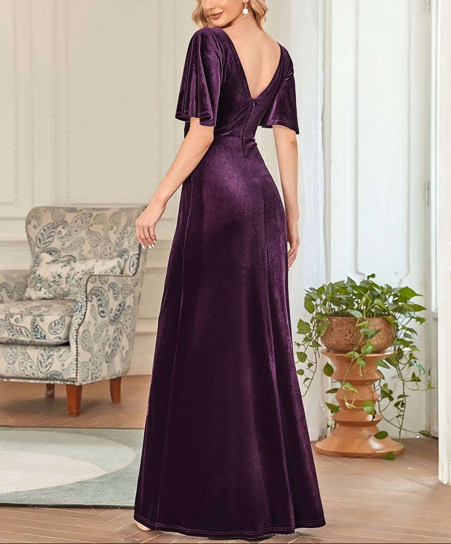 Woman wearing a purple velvet dress in a room with a chair and plant.