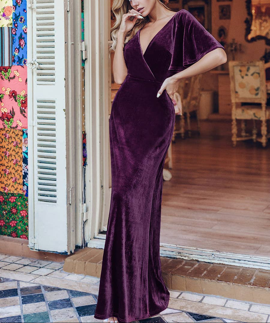 Woman wearing a purple velvet dress standing in a room with colorful decor.